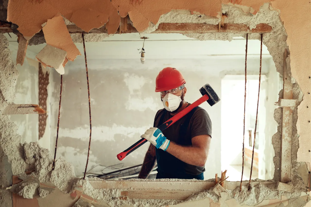 Bauarbeiter mit Vorschlaghammer beim Rückbau einer nichttragenden Wand